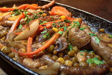 Hungarian frying pan (pork and beef sausages stewed with vegetables in dark beer) on a large wooden board. Tasty and healthy food. Close-up.