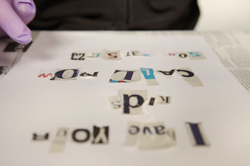 Criminal in hooded shirt preparing ransom letter from newspaper