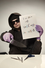 Criminal in hooded shirt preparing ransom letter from newspaper