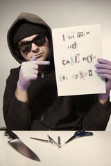 Criminal in hooded shirt preparing ransom letter from newspaper