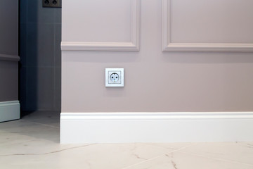 electrical outlet on the brown wall above the baseboard and marble floor