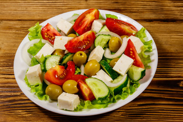 Greek salad with fresh vegetables, feta cheese and green olives on wooden table