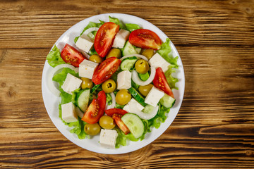 Greek salad with fresh vegetables, feta cheese and green olives on wooden table. Top view