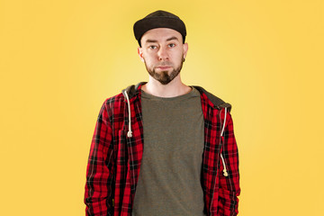 Fototapeta na wymiar Caucasian bearded man, wearing a black cap and checked shirt. Hipster. Yellow background. Copy space