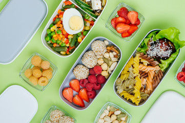 Plastic lunch boxes with healthy food on light green background