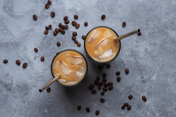 Two cold coffee in a glass cup with a metal straw, coffee beans on a gray concrete background