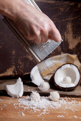 Close up of coconut with white pulp, grater with coconut chip and white candies on wooden background..