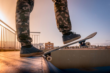 Primer plano de las piernas de un joven skater con su tabla en la parte superior de una rampa al...