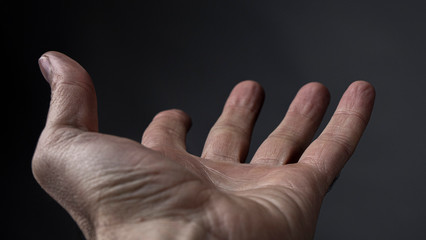 Man's Hand Begs For Something On A Dark Background. Open Man's Cupped Hand Begging For Alms On Gray Background. High Quality Photo