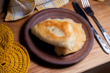 Clay plate of fried meat pies with cutlery on wooden table.