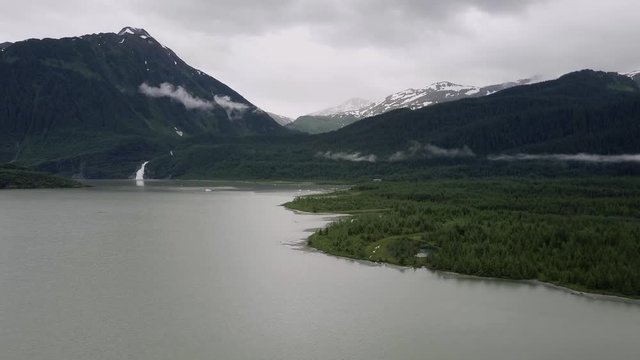 Wisps of clouds and fog over the deep green mountains near Mendenhall Lake and Nugget Falls in Alaska from aerial drone