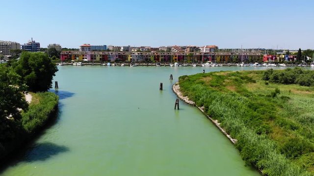 Caorle Italy boat canal in Porto Santa Margherita leading to the marina with colorful beach homes, Aerial drone flyover shot
