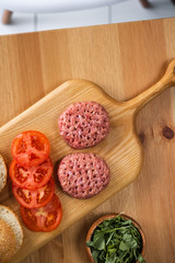 Buns, raw beef cutlets, tomatoes and herbs for burgers cooking