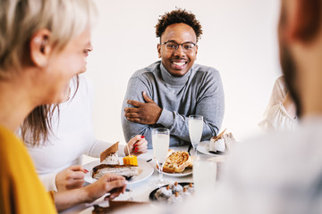 Smiling attractive african american man sitting at dinning table with friends for lunch, smiling and looking at camera.