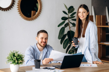 Fototapeta premium Young creative office workers at the workplace drink coffee and smiling