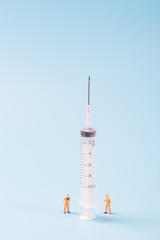 Syringe and miniature human and oral medicine and thermometer macro closeup on blue background