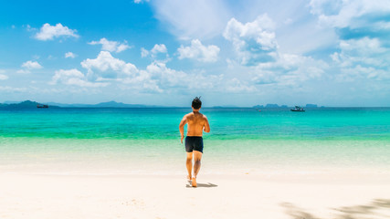 Wellness fit body young man traveler running on beautiful nature white sandy beach at sunny day, Active male joy travel Phuket Trang Thailand fun beach, Summer holidays vacation background copy space