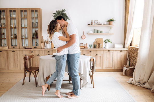 Couple in love in stylish casual wear is kissing in their interior kitchen at home