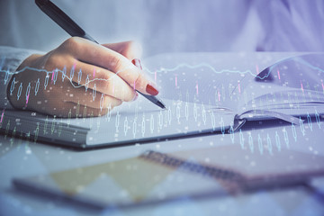Multi exposure of woman's hands making notes with forex graph hologram. Concept stock market...