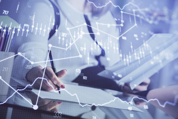 A woman hands writing information about stock market in notepad. Forex chart holograms in front. Concept of research.