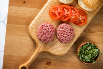 Buns, raw beef cutlets, tomatoes and herbs for burgers cooking
