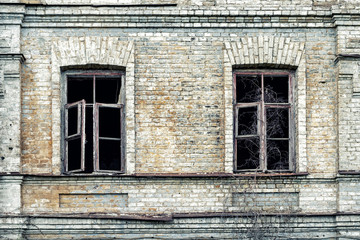Old shabby ruined abandoned brick building wall facade with two wooden brocken glass windows and dark black background. Shattered grunge aged house exterior. Poverty, decay and breakdown concept