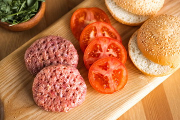 Buns, raw beef cutlets, tomatoes and herbs for burgers cooking