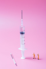 Syringe and miniature human and oral medicine and thermometer macro closeup on pink background