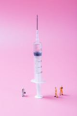 Syringe and miniature human and oral medicine and thermometer macro closeup on pink background