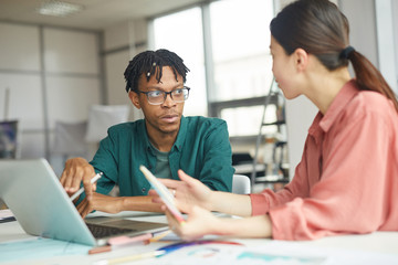 Obraz premium African young businessman sitting at the table with young businesswoman and they discussing online presentation on laptop