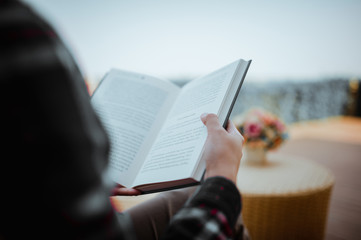 Young woman sitting in backyard, reading book and relaxing. Blurred background.Horizontal, film effect.