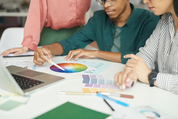 Close-up of team of designer pointing at colored pattern while working in team at the table at office