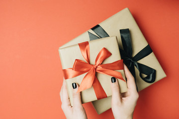 Partial view of woman tying ribbon on gift box isolated on red
