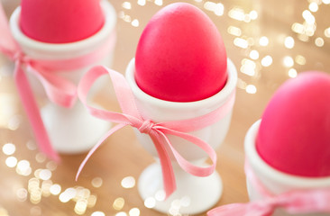 easter and holidays concept - pink colored eggs in ceramic cup holders with ribbon on table