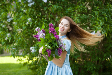 Beautiful woman in a blue summer dress with lilac flowers in a blooming garden. Spring Blossom.