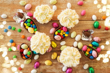 easter, food and holidays concept - frosted cupcakes with chocolate eggs and candies on wooden table