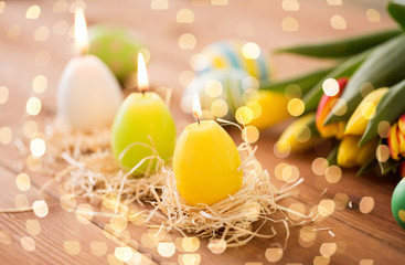 easter, holidays, tradition and object concept - three burning candles in shape of eggs and tulip flowers on wooden table