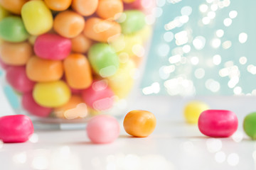 food, confectionery and sweets concept - close up of glass jar with colorful candy drops over lights on blue background