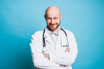 Attractive friendly bald bearded smiling doctor looking at camera isolated on blue background