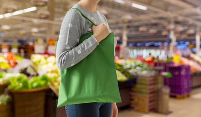 consumerism and eco friendly concept - woman with green reusable canvas bag for food shopping over...