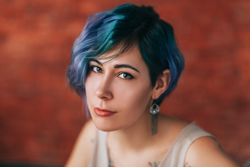 Beautiful young woman with stylish green and purple hair and tattoo on her body posing over red brick wall. Hair coloring, make-up, Tattoo.