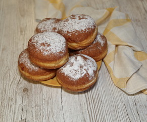 Donuts sprinkled with powdered sugar, some in soft focus, close up on wooden table, kitchen cloth