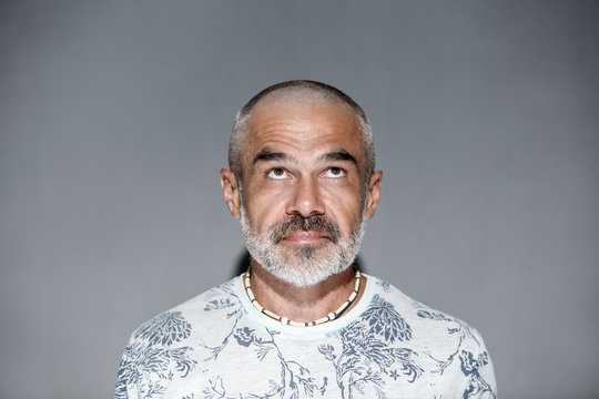 Friendly mature man with short hair and white grey beard  looking upwards over gray wall