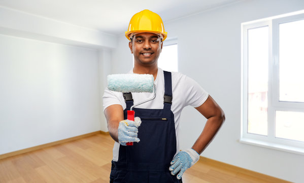 repair, construction and building - happy smiling indian builder or painter in helmet with paint roller over empty home or apartment room background