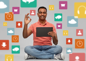 technology, media and people concept - happy indian man with tablet computer sitting on floor over app icons on grey background
