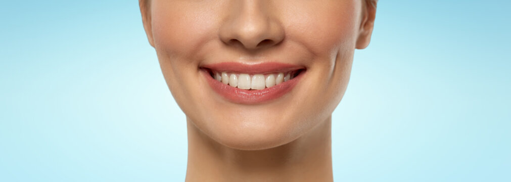 beauty, dental care and teeth whitening concept - close up of beautiful young woman face with white smile over blue background