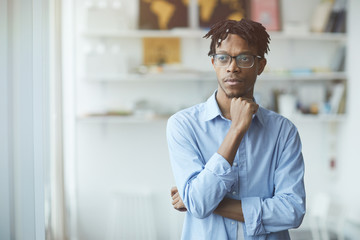 Obraz premium Pensive African businessman in eyeglasses standing at office and looking away he thinking about something