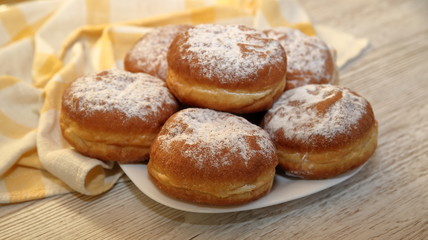 Obraz na płótnie Canvas Donuts sprinkled with powdered sugar, some in soft focus, close up on wooden table, kitchen cloth
