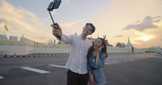 Girl and boyfriend travel in Bangkok, Thailand. sweet couple using mobile phone selfie while spending sweet time in holiday trip over the sunset background in slow motion. Sweet couple travel in the c