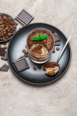 Classic tiramisu dessert in a glass cup, pieces of chocolate on concrete background